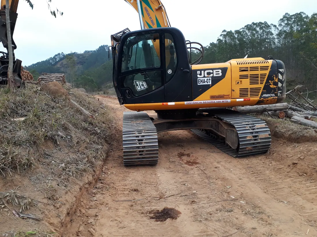 Escavadeira hidráulica em operação em estrada de terra em área florestal