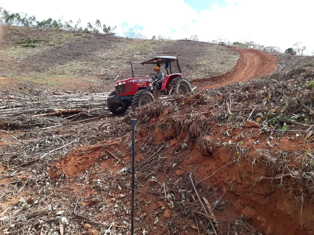 Trator agrícola vermelho trabalhando em encosta de terra